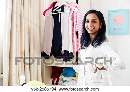 Picture - Tilburg, Netherlands. Young, dark skinned woman cleaning up her wardrobe closet in her bedroom.. Fotosearch