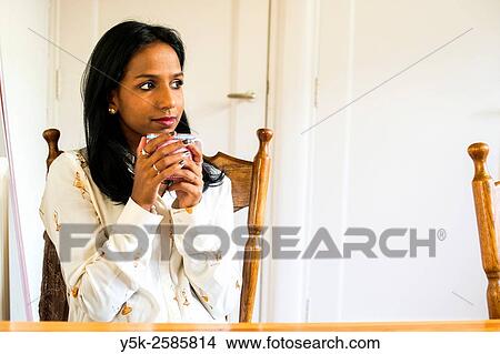 Tilburg, Netherlands. Young, dark colored woman drinking a warm cup of thee, while sitting at her kitchen table. View Large Photo Image Picture - Tilburg, Netherlands. Young, dark colored woman drinking a warm cup of thee, while sitting at her kitchen table.. Fotosearch