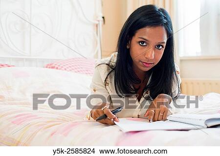 Tilburg, Netherlands. Young, dark skinned woman reading back from her diary, whily stretched out on her bed. View Large Photo Image Picture - Tilburg, Netherlands. Young, dark skinned woman reading back from her diary, whily stretched out on her bed.. Fotosearch