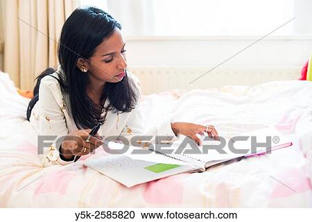 Tilburg, Netherlands. Young, dark skinned woman reading back from her diary, whily stretched out on her bed. View Large Photo Image Stock Image - Tilburg, Netherlands. Young, dark skinned woman reading back from her diary, whily stretched out on her bed.. Fotosearch