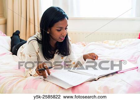 Tilburg, Netherlands. Young, dark skinned woman reading back from her diary, whily stretched out on her bed. View Large Photo Image Stock Image - Tilburg, Netherlands. Young, dark skinned woman reading back from her diary, whily stretched out on her bed.. Fotosearch
