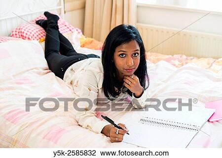 Tilburg, Netherlands. Young, dark skinned woman reading back from her diary, whily stretched out on her bed. View Large Photo Image Stock Image - Tilburg, Netherlands. Young, dark skinned woman reading back from her diary, whily stretched out on her bed.. Fotosearch