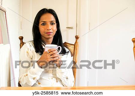 Tilburg, Netherlands. Young, dark colored woman drinking a warm cup of thee, while sitting at her kitchen table. View Large Photo Image Stock Photography - Tilburg, Netherlands. Young, dark colored woman drinking a warm cup of thee, while sitting at her kitchen table.. Fotosearch