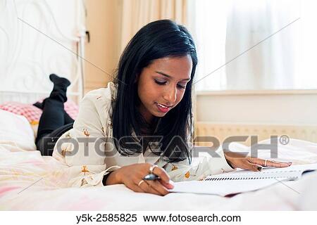 Tilburg, Netherlands. Young, dark skinned woman reading back from her diary, whily stretched out on her bed. View Large Photo Image Stock Photography - Tilburg, Netherlands. Young, dark skinned woman reading back from her diary, whily stretched out on her bed.. Fotosearch