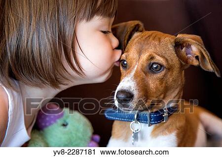 Stock Image - Toddler girl kissing her puppy dog.. Fotosearch