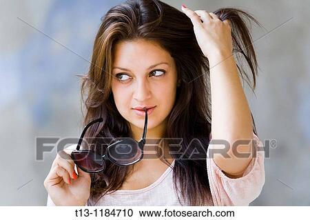 Stock Image - Watching away with sunglasses in hands young woman. Fotosearch