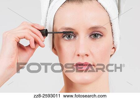 Stock Image - Woman applying mascara after shower with white towel on her head.. Fotosearch