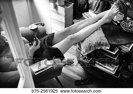 Stock Photography - Woman sitting in an armchair, barefoot with feet up on a table, in a relax position, handling a mobile phone in a town house. Mahn, Menorca, Balearic Islands, Spain, Europe.. Fotosearch