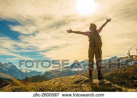 Woman with back pack and outstretched arms enjoy panoramic view over snow-capped mountain in a sunny summer day in Grisons, Switzerland. View Large Photo Image Stock Photo - Woman with back pack and outstretched arms enjoy panoramic view over snow-capped mountain in a sunny summer day in Grisons, Switzerland.. Fotosearch