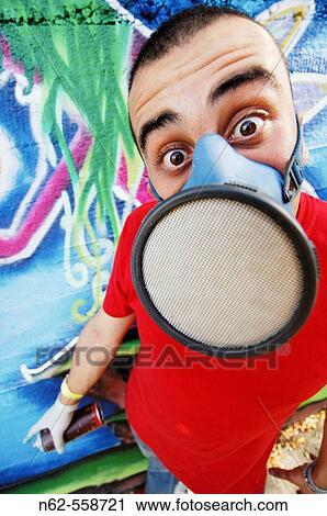 Stock Image - Writers with surprised expression in front of his newly colorful mural wearing face mask and latex gloves he is holding a spray can. Fotosearch