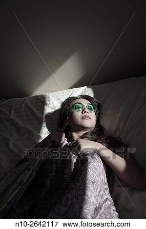 Young Asian woman lying on her bed, wearing colored glasses. View Large Photo Image Stock Photo - Young Asian woman lying on her bed, wearing colored glasses.. Fotosearch