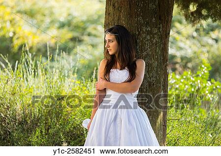 Stock Image - Young bride hiding behind tree. Fotosearch
