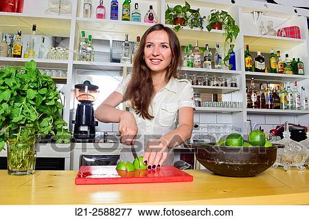 Stock Photo - Young female bartender cutting lemons, preparing cocktails. Woman barman at work.. Fotosearch