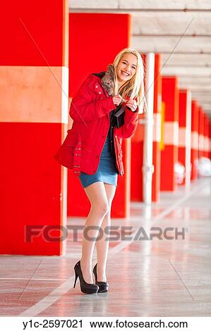 Stock Image - Young lady is happy in empty Red-walled parking-lot. Fotosearch