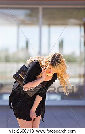 Stock Photo - Young lady is pulling down of her dress. Fotosearch
