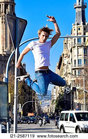 Young man doing a jump on a street. He is dressed in a white shirt, jeans and sneakers. Barcelona, Catalonia, Spain. View Large Photo Image Stock Photo - Young man doing a jump on a street. He is dressed in a white shirt, jeans and sneakers. Barcelona, Catalonia, Spain.. Fotosearch
