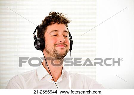 Young man listening to music on his headphones in the interior of a house. View Large Photo Image Picture - Young man listening to music on his headphones in the interior of a house.. Fotosearch
