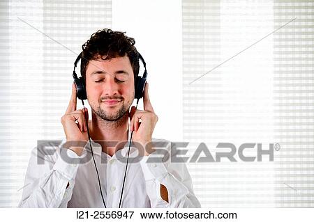 Young man listening to music on his headphones in the interior of a house. View Large Photo Image Stock Photo - Young man listening to music on his headphones in the interior of a house.. Fotosearch