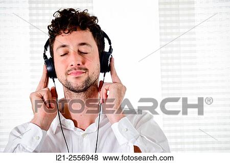 Young man listening to music on his headphones in the interior of a house. View Large Photo Image Stock Photo - Young man listening to music on his headphones in the interior of a house.. Fotosearch