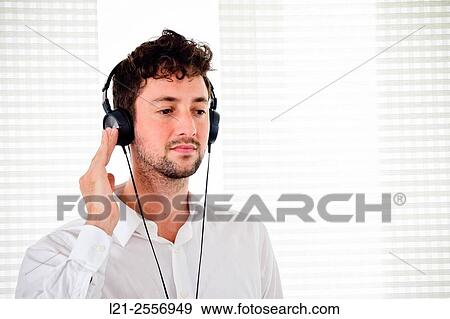 Young man listening to music on his headphones in the interior of a house. View Large Photo Image Stock Photo - Young man listening to music on his headphones in the interior of a house.. Fotosearch