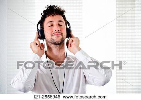 Young man listening to music on his headphones in the interior of a house. View Large Photo Image Stock Photograph - Young man listening to music on his headphones in the interior of a house.. Fotosearch