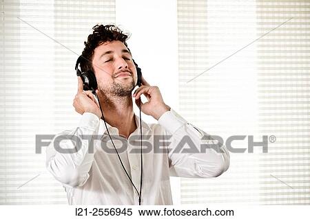 Young man listening to music on his headphones in the interior of a house. View Large Photo Image Stock Photography - Young man listening to music on his headphones in the interior of a house.. Fotosearch