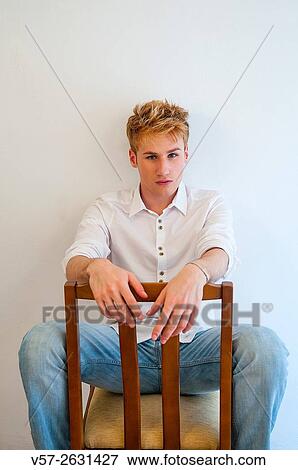 Young man sitting astride on a chair, looking at the camera. View Large Photo Image Stock Photo - Young man sitting astride on a chair, looking at the camera.. Fotosearch