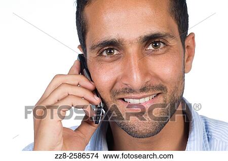 Young Middle Eastern man talking on mobile phone against a white background. View Large Photo Image Picture - Young Middle Eastern man talking on mobile phone against a white background.. Fotosearch
