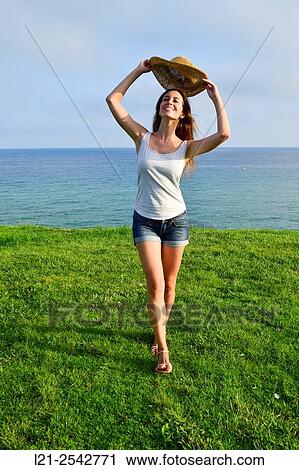 Young woman in summer clothes and straw hat standing on the grass near the sea. She is dressed with short jeans and a white blouse. View Large Photo Image Stock Image - Young woman in summer clothes and straw hat standing on the grass near the sea. She is dressed with short jeans and a white blouse.. Fotosearch