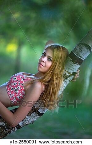 Stock Image - Young woman is lying on curved tree in forest. Fotosearch