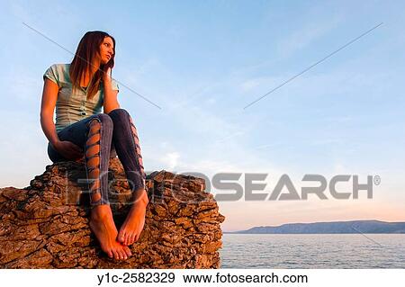 Stock Photo - Young woman is watching sunset sad and lonely. Fotosearch