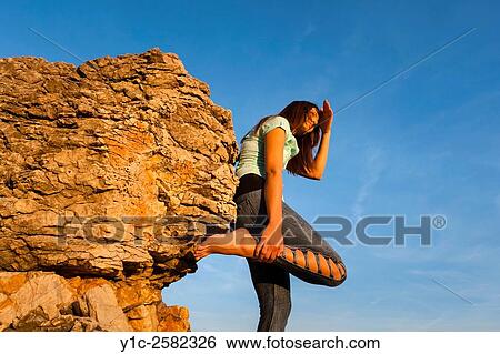 Stock Photograph - Young woman is watching sunset hand-holding leg. Fotosearch