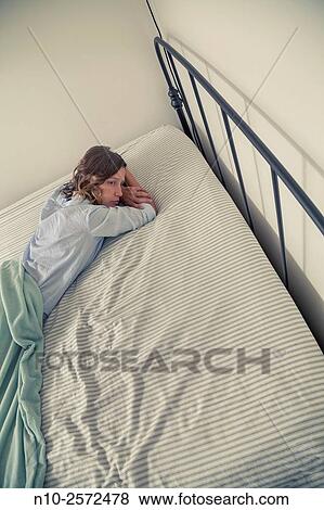 Stock Photo - Young woman lying on her bed.. Fotosearch
