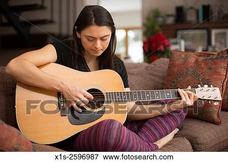 Young woman plays a blond acoustic guitar using her fingers to strum the guitar strings. View Large Photo Image Stock Photo - Young woman plays a blond acoustic guitar using her fingers to strum the guitar strings.. Fotosearch