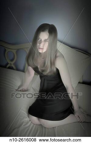 Stock Photo - Young woman, wearing a black dress, sitting on her bed.. Fotosearch
