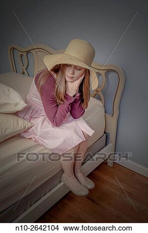 Picture - Young woman, wearing a hat, sitting on a bed.. Fotosearch