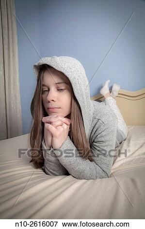 Young woman wearing a sweatshirt and hoodie, lying on her bed. View Large Photo Image Stock Photo - Young woman wearing a sweatshirt and hoodie, lying on her bed.. Fotosearch