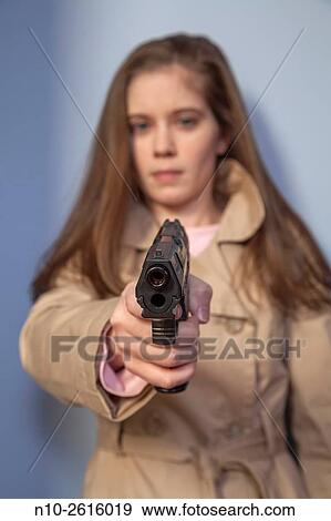 Stock Photo - Young woman, wearing a trench coat, holding a gun.. Fotosearch