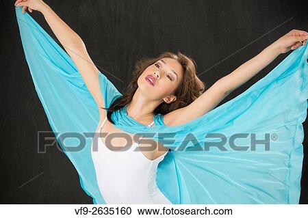 Stock Image - Beautiful young woman dancer in light blue cape and white leotard, half length with arms flung out, like wings, against black background, horizontal image.. Fotosearch
