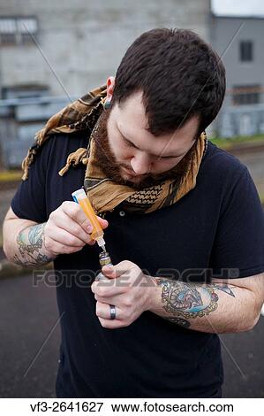 Stock Photo - EUGENE, OR - MARCH 20, 2016: Urban portrait of a bearded hipster man with tattoos vaping using a custom mod vape device.. Fotosearch