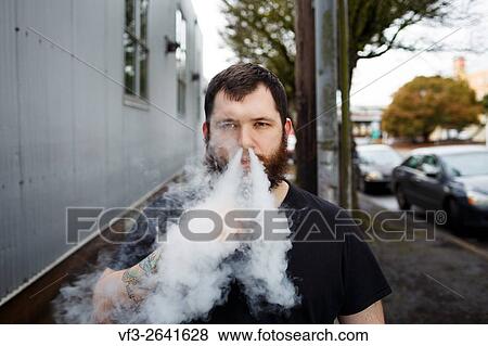 EUGENE, OR - MARCH 20, 2016: Urban portrait of a bearded hipster man with tattoos vaping using a custom mod vape device. View Large Photo Image Stock Photo - EUGENE, OR - MARCH 20, 2016: Urban portrait of a bearded hipster man with tattoos vaping using a custom mod vape device.. Fotosearch