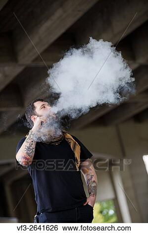 EUGENE, OR - MARCH 20, 2016: Urban portrait of a bearded hipster man with tattoos vaping using a custom mod vape device. View Large Photo Image Stock Photograph - EUGENE, OR - MARCH 20, 2016: Urban portrait of a bearded hipster man with tattoos vaping using a custom mod vape device.. Fotosearch