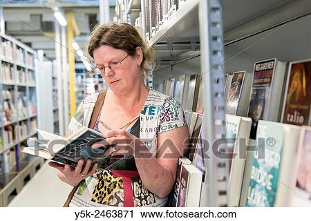 Gouda, Netherlands. Middle aged woman choosing a book to read from the library shelves. View Large Photo Image Stock Image - Gouda, Netherlands. Middle aged woman choosing a book to read from the library shelves.. Fotosearch