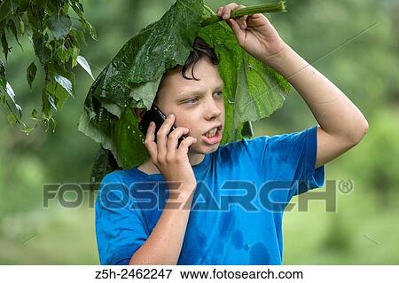Stock Photo - Russian Federation. Belgorod region. The boy in the rain uryvshiysya leaves of the plant.. Fotosearch