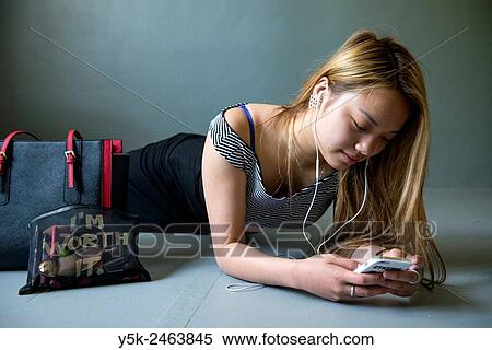 Tilburg, Netherlands. Female Chinese teenager playing with her smartphone, while lying on the studio floor. View Large Photo Image Stock Photography - Tilburg, Netherlands. Female Chinese teenager playing with her smartphone, while lying on the studio floor.. Fotosearch