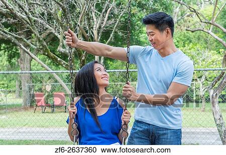 Stock Image - Vietnamese-American couple dating at playground with swings and having fun MR-6 MR-8 Model released.. Fotosearch