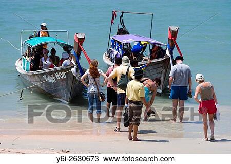 Stock Image - Visitors board long tail boats on Ao Nang Beach to get to other beaches and resorts Thailand.. Fotosearch