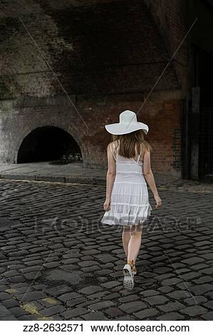 Stock Image - Woman walking on a cobbled road.. Fotosearch