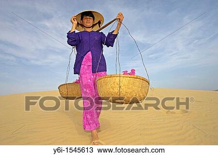 Woman with conical hat carries flowers in pannier baskets across sand dunes near Mui Ne Vietnam View Large Photo Image Stock Image - Woman with conical hat carries flowers in pannier baskets across sand dunes near Mui Ne Vietnam. Fotosearch