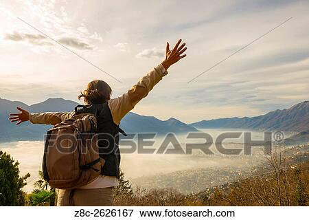 Woman with outstretched arms and backpack enjoy panoramic view with sea of fog over alpine lake Maggiore with mountain in Ticino, Switzerland. View Large Photo Image Stock Photo - Woman with outstretched arms and backpack enjoy panoramic view with sea of fog over alpine lake Maggiore with mountain in Ticino, Switzerland.. Fotosearch